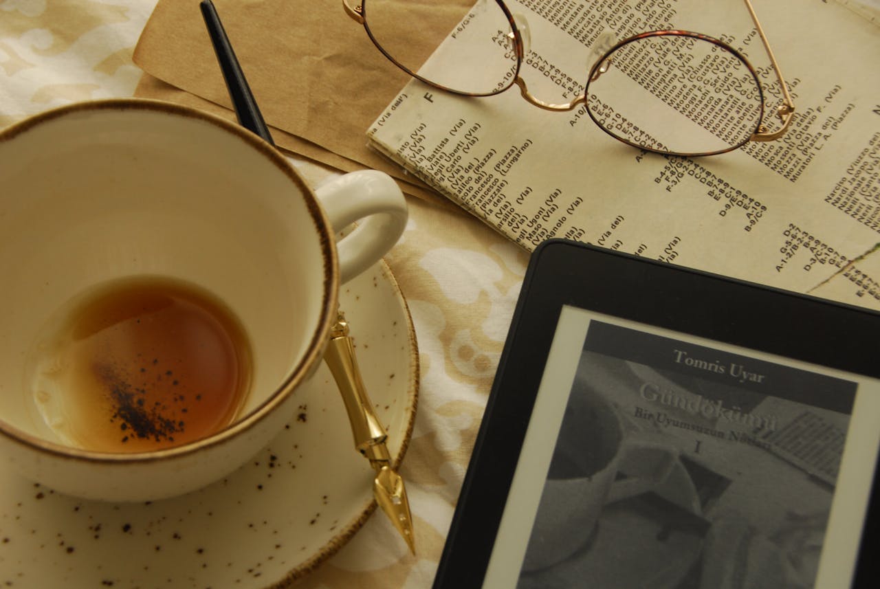Cozy flat lay scene with tea, eyeglasses, and e-reader on a table.